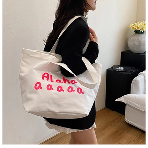 Detailed close-up of large white canvas tote bag with pink Alaha lettering and straps