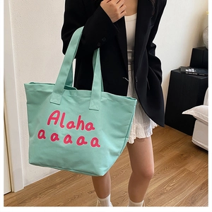 Close-up of mint green canvas tote bag with pink artistic lettering and wide shoulder strap