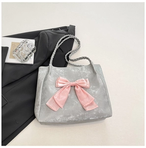 Detail of grey tote bag featuring a large pink bow and braided rope handles on a stylish desk