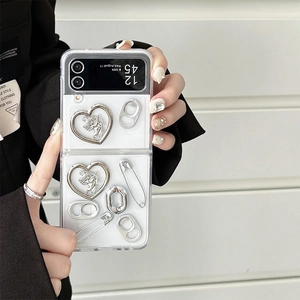 Close-up of heart charm and safety pin detail on a white Samsung Z Flip 6 case