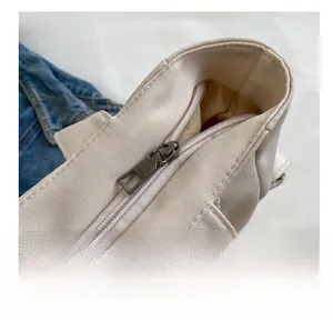 Detailed close-up of smooth metal zipper closure on off-white canvas tote bag