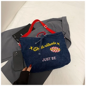 Detail of dark wash denim tote with Chill vibes embroidery and red shoulder strap