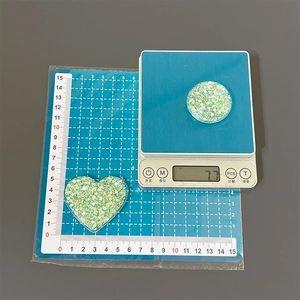 Green glitter resin heart and round phone stand components on a scale showing 7.7g weight