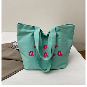 Detailed view of mint green canvas tote bag featuring large pink letter print and long straps