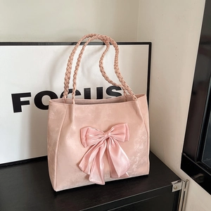 Pink tote bag with large bow and braided handle in a minimalist indoor setting