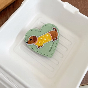 Detail of heart-shaped leather phone grip featuring embroidered puppy and slogan