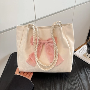 Elegant cream tote bag with large pink bow and woven handles on a stylish wooden desk