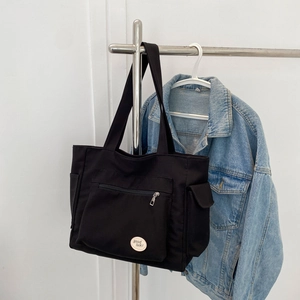 Black high-capacity canvas tote bag with front zipper pocket and side flap compartment