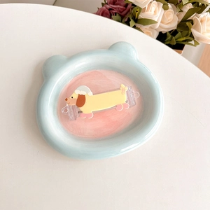 Close-up of a yellow cartoon dachshund hair clip in a ceramic tray with floral accents