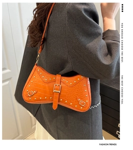 Detail view of bright orange crocodile pattern dumpling bag with gold rivets and metallic buckle