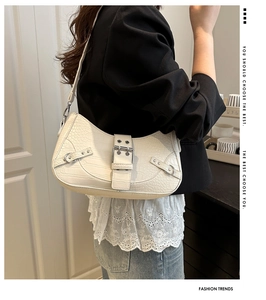 Detail of a chic cream crocodile-patterned underarm bag with metal buckle on the strap