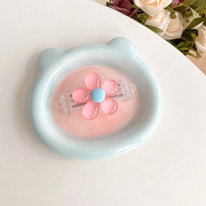 Detailed close-up of a cute pink flower phone back clip displayed on a blue bear dish
