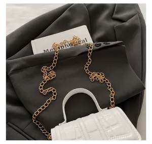 Macro detail of the golden metal chain strap and stone texture on a white mini square handbag