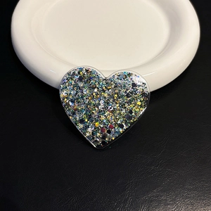 Macro shot of heart-shaped glitter phone stand with colorful sequins on ceramic tray