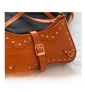 Detail view of orange crocodile texture leather with gold rivets and metallic buckle hardware