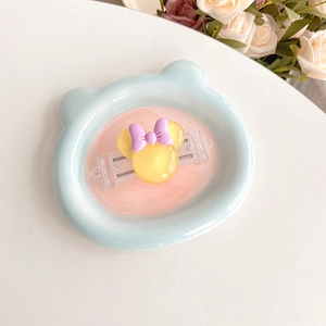 Detail of yellow cartoon mouse phone back clip with purple bow on a light blue tray