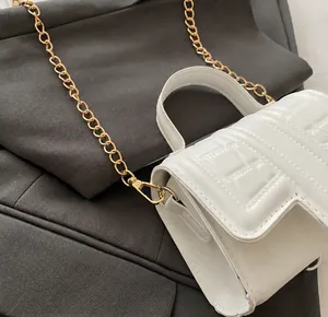 Detail shot of the gold hardware hook and chain on a white stone-textured mini bag