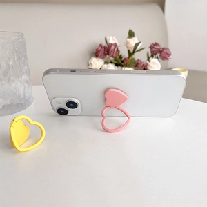 Detail view of pink and yellow heart-shaped phone ring stands on a white smartphone