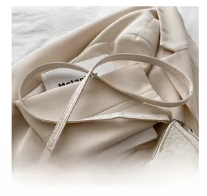 Detail of adjustable silver buckle on cream faux crocodile skin strap of a shoulder bag