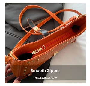 Detail view of smooth golden zipper and orange crocodile embossed leather texture