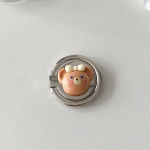 Detail view of a silver metal phone ring stand with a 3D cartoon bear and a bow decoration
