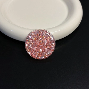 Macro shot of circular pink glitter resin phone grip on white ceramic and black leather