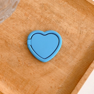 Detail view of a matte blue heart-shaped phone ring holder resting on a wooden tray