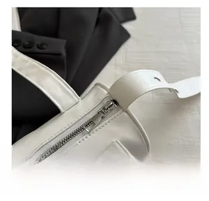 Detailed close-up of the smooth silver zipper and stitching on a white cylinder shoulder bag