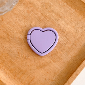 Detail of a purple heart-shaped foldable mobile phone ring holder on a wood tray