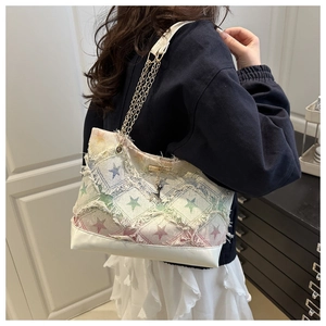 Detail of denim tote bag with star patterns, frayed edges and gold chain strap