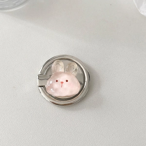 Detail of pink resin bunny phone ring holder with silver metal base on a grey surface