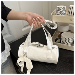 Detailed view of a white cylindrical handbag featuring silver hardware and a bow charm