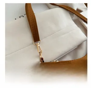 Close-up of a golden lobster clasp on a brown suede shoulder bag with fringe
