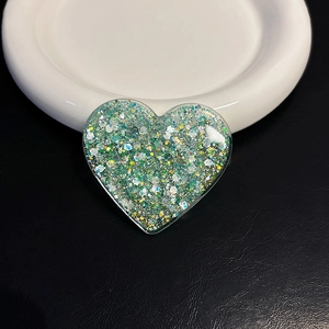 Detail of heart-shaped glitter phone socket with green and silver sequins on a white plate
