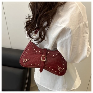 Detail of burgundy crocodile-embossed baguette bag with golden studs and metal buckles