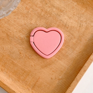 Close-up of a pink heart-shaped phone ring holder on a rustic wooden background