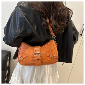 Detail of orange crocodile pattern saddle bag with silver buckle on a model's shoulder