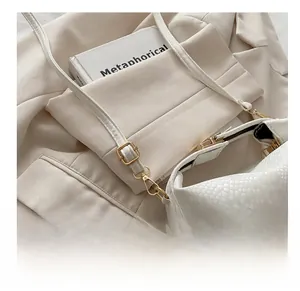 Detail of adjustable golden metal buckle and spring hook on white snakeskin textured strap
