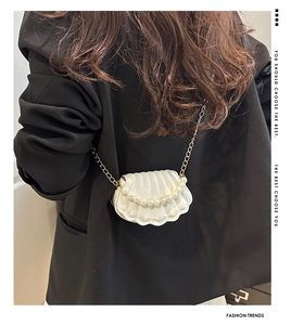 Detail of white shell-shaped pearl bag with golden chain on black blazer outfit