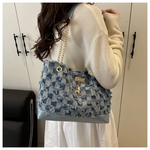 Detail of denim checkerboard tote bag with fringe edges and a golden deer pendant