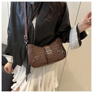 Detail of dark brown faux-crocodile baguette bag with silver metal buckle and rivets
