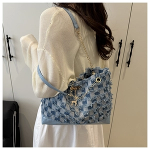 Detail of blue checkered denim tote bag with frayed edges and golden chain strap