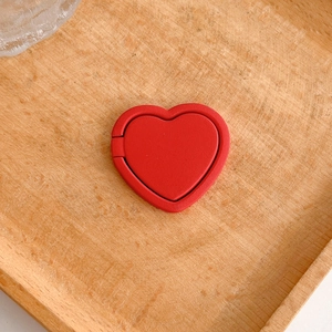 Close-up of a matte red heart-shaped phone ring stand on a wooden surface
