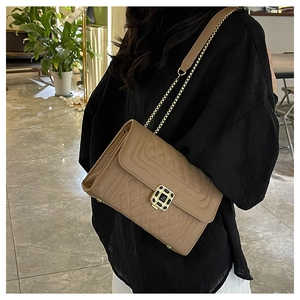 Detail of khaki quilted chain crossbody bag with golden geometric clasp on a model