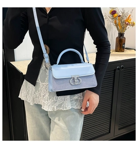 Detail shot of light blue crossbody bag featuring vintage metal buckle and leather strap