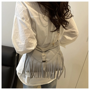 Detail of light gray suede crossbody bag with long tassels and metallic buckle on model