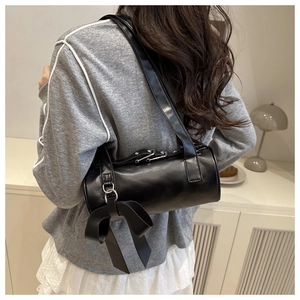 Detail of a black cylinder shoulder bag featuring a large decorative bow on the side