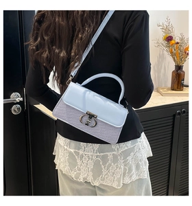 Model wearing a light blue contrast shoulder bag with metal buckle in a cozy home setting