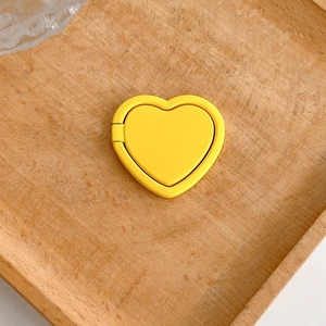 Detailed close-up view of a matte yellow heart-shaped phone ring holder stand on wood