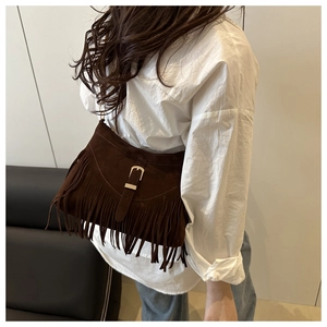 Detailed view of a dark brown suede tassel crescent bag on a model in a minimal setting